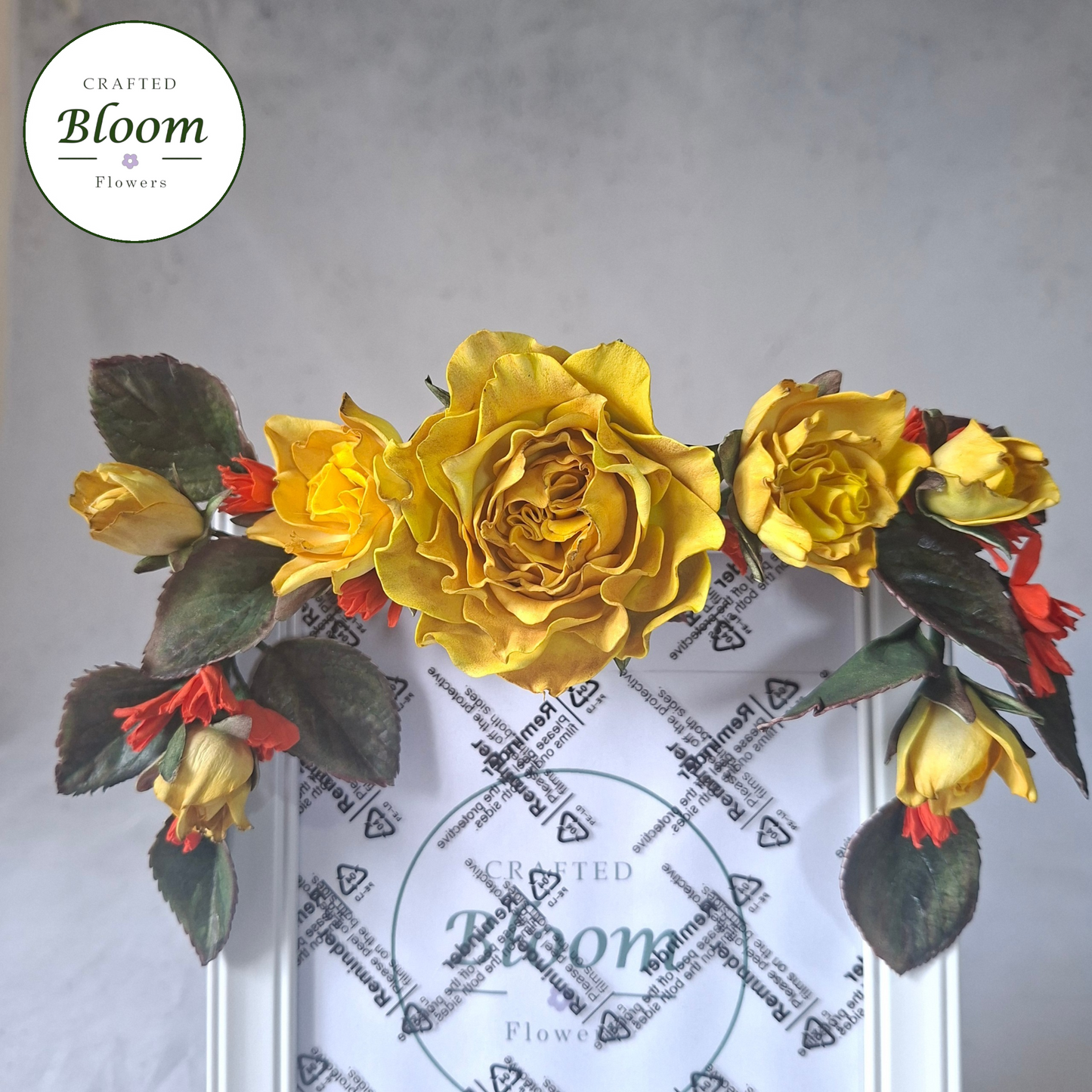 Close-up of handcrafted yellow rose and red but floral arrangement on white phot frame