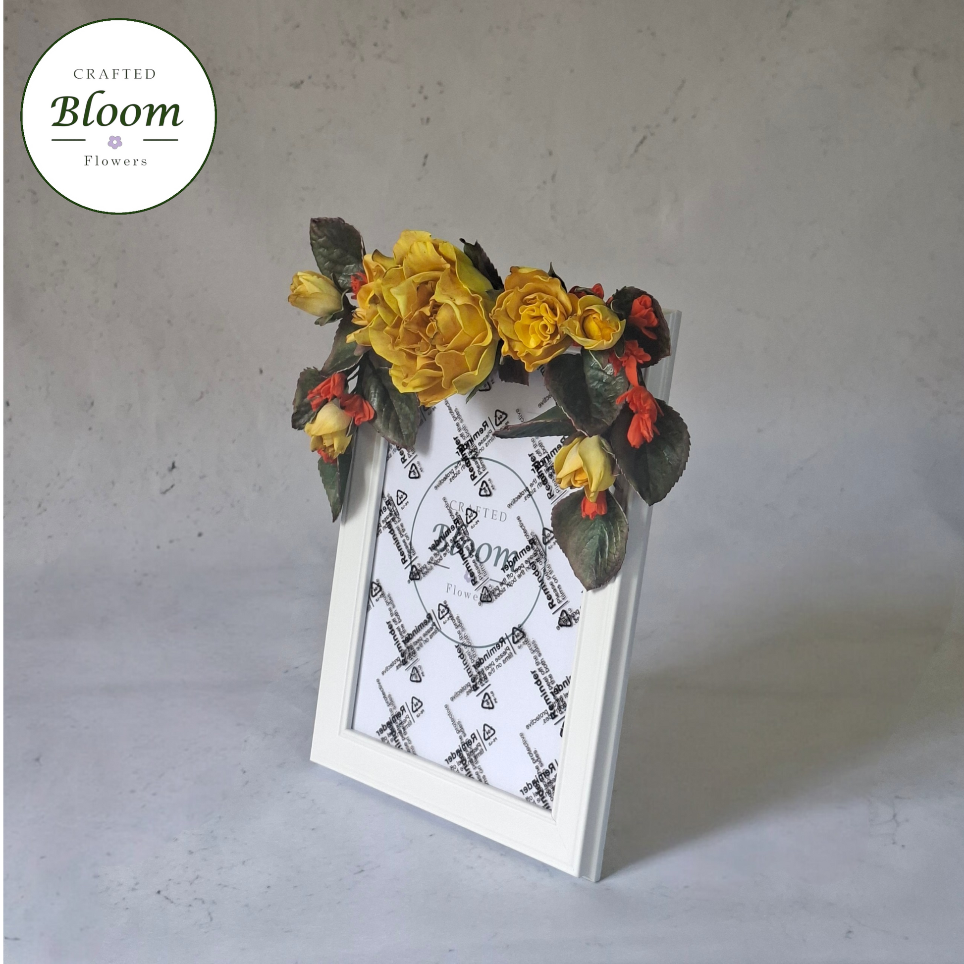 Close-up of handcrafted yellow rose and red but floral arrangement on white photo frame