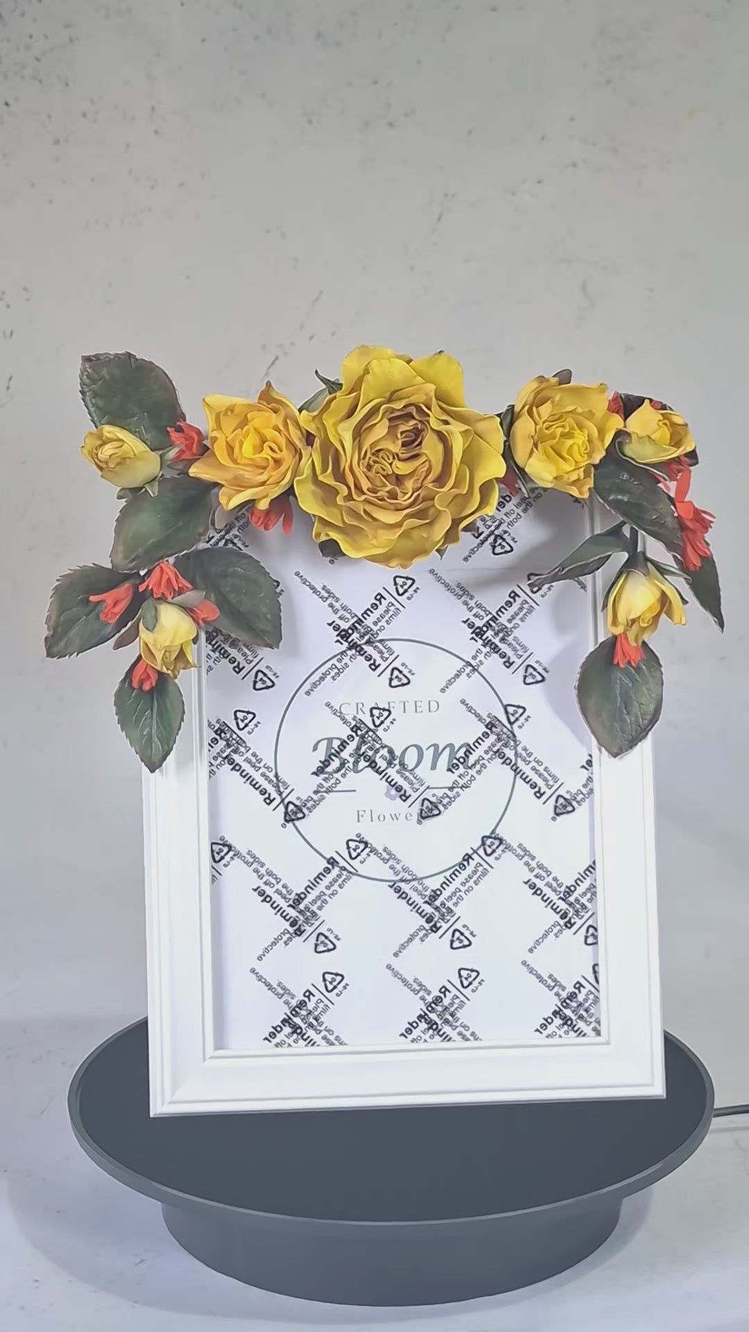 Detailed view of handmade yellow roses, rosebuds, and dark green leaves adoring a white frame corner